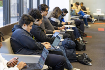 Students sit, using laptops.