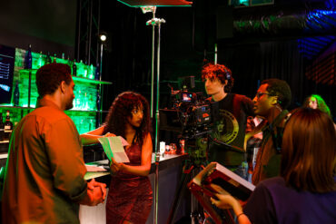 A director works with actors on a nightclub set