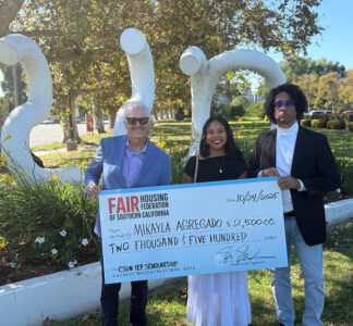 Three people stand in front of the CSUN sculpture holding a large, ceremonial check.