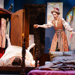 An actor reacts in surprise as another actor appears to fall to the floor in a castle bedroom.