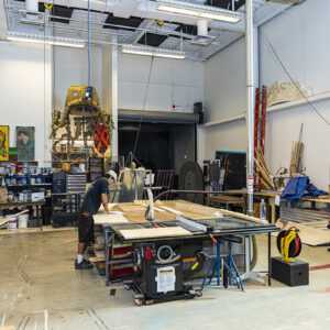 A wide shot of a student working in a workshop where theater backgrounds are built.