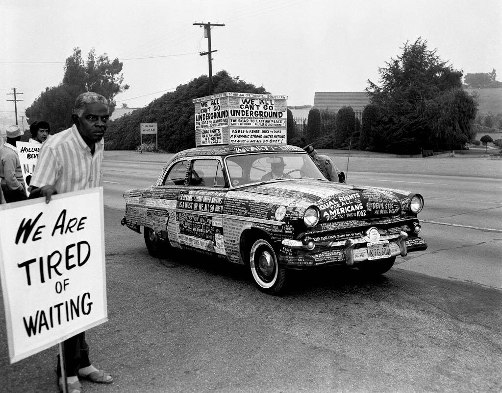 Man with sign standing next to car covered with protest signs.