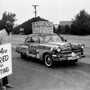 Man with sign standing next to car covered with protest signs.
