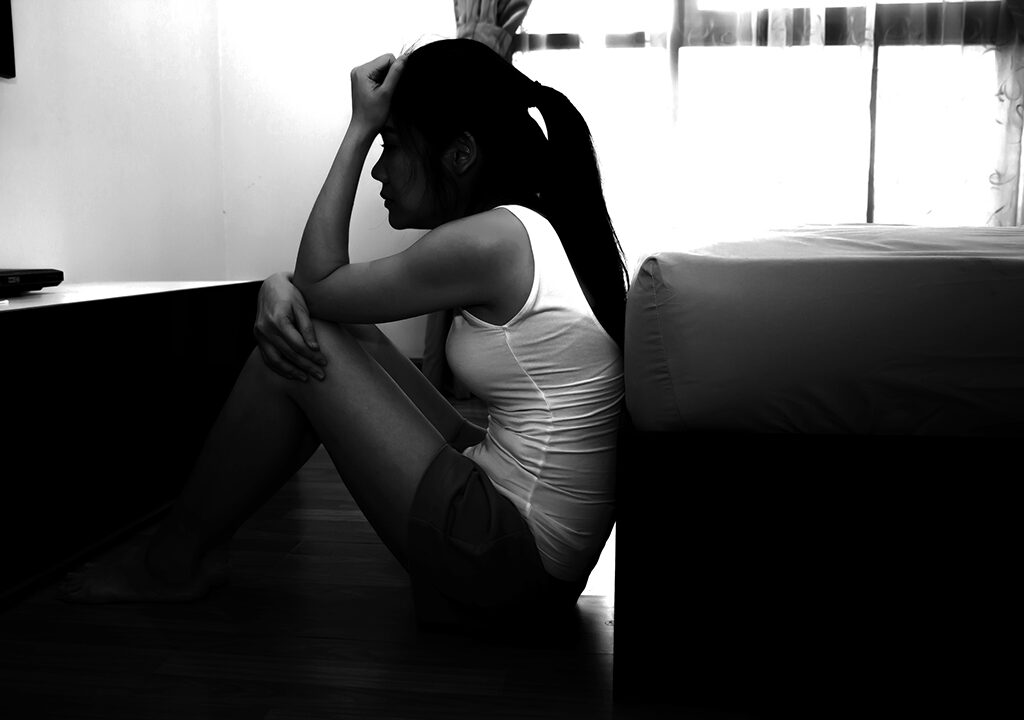 Woman, in shadows, sitting on floor in distress.