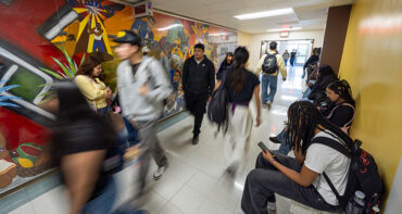Students walk through a hallway, with a mural in the background.