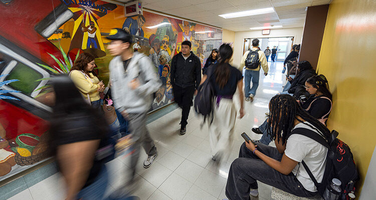 Students walk through a hallway, with a mural in the background.