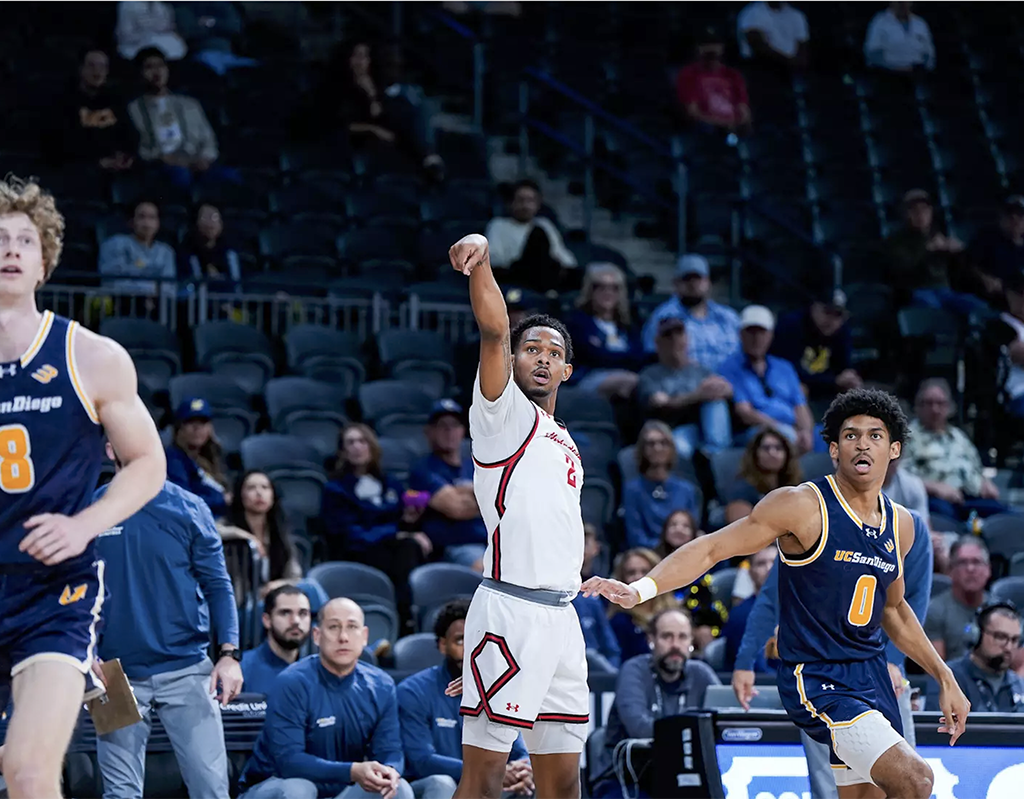 A male basketball player and two defenders watch after he releases a 3-point shot.