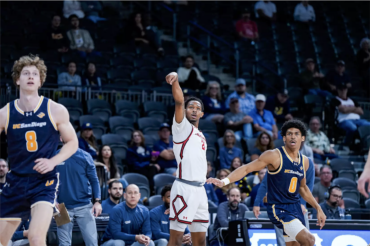 A male basketball player and two defenders watch after he releases a 3-point shot.