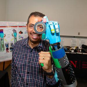 Peter Bishay uses a prosthetic arm to hold a roll of tape up to his eye.
