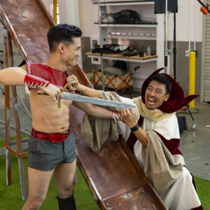 Actors dressed as Flash Gordon and Ming the Merciless struggle to keep straight faces during an action sequence.