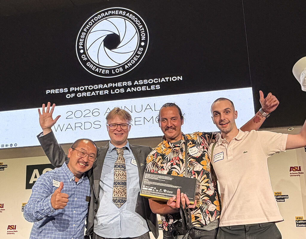Four men pose together, smiling for the camera with a screen in the background.
