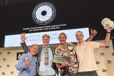 Four men pose together, smiling for the camera with a screen in the background.