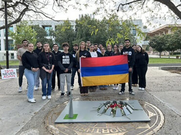 A group of Armenian students hold an Armenian flag in front of a wooden replica of an Armenian Genocide memorial eternal flame. They are standing in Matador Square.