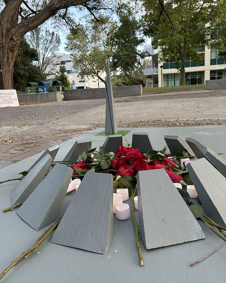 A wooden replica of an Armenian Genocide memorial eternal flame is covered with red roses and battery-powered candles. It is sitting in the middle of Matador Square.