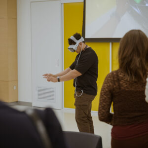 A person in an Apple Vision Pro headset at the front of a crowded room.