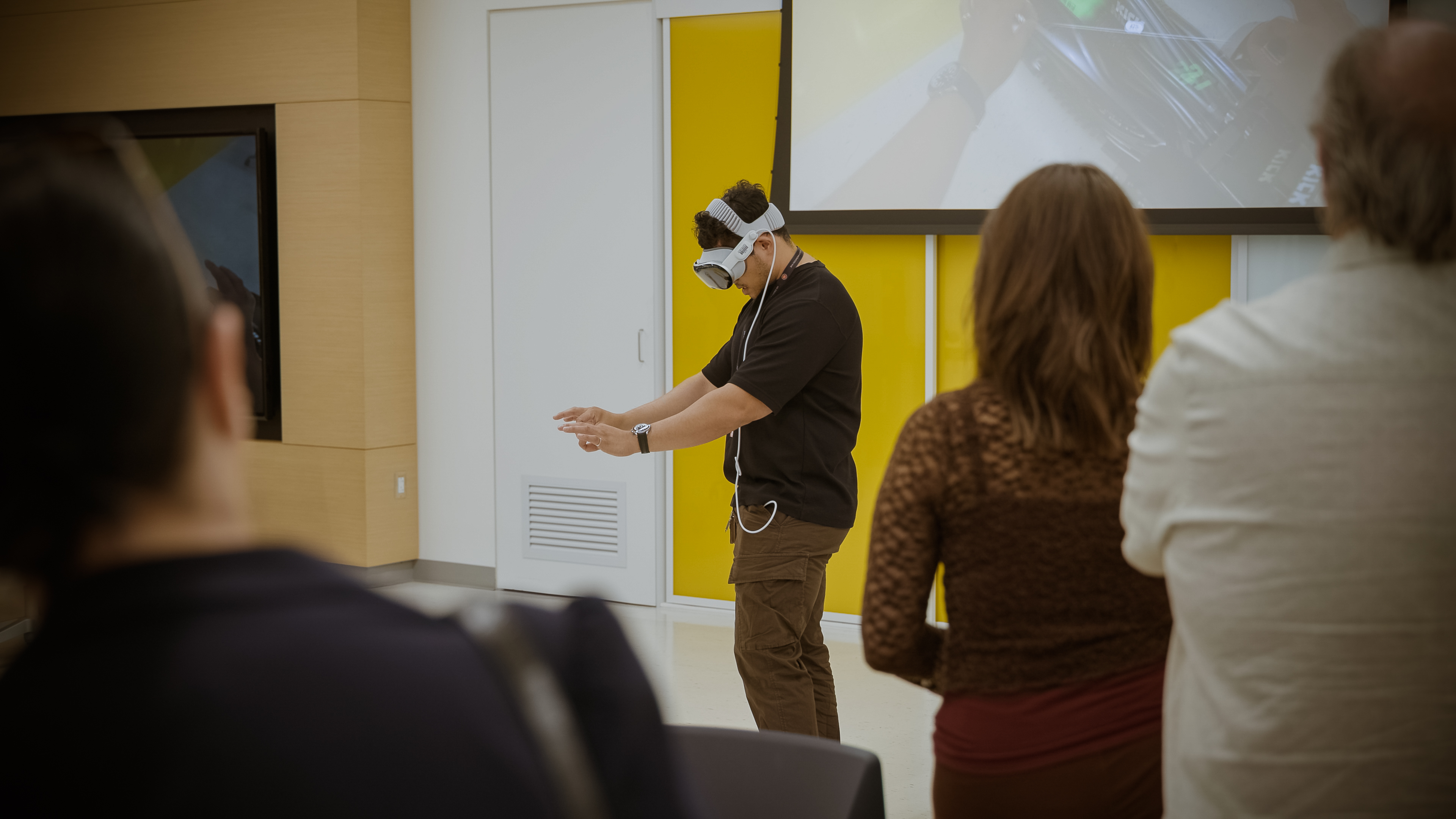 A person in an Apple Vision Pro headset at the front of a crowded room. 