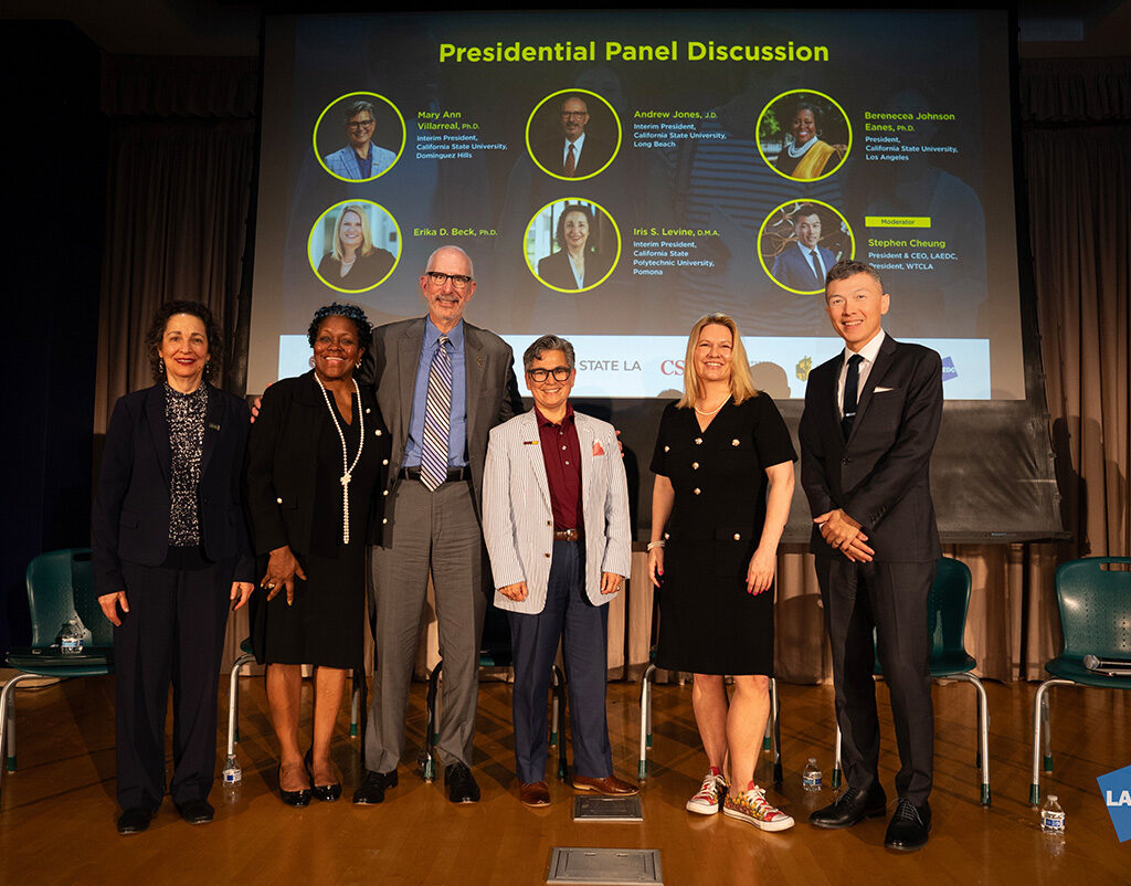 Six people stand on stage and pose for a group photo.