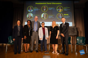 Six people stand on stage and pose for a group photo.