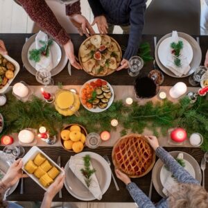 Top view of hands of family members holding plates with homemade food and desserts while serving festive table before Christmas dinner. Credit: shironosov via IStock