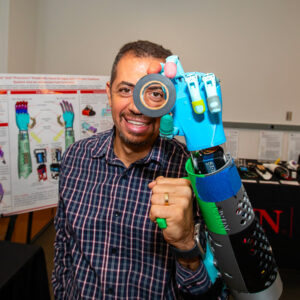 Peter Bishay holds up a roll of tape to his eye with a prosthetic hand.