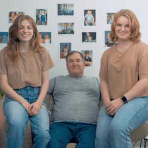 Haily, Steve and Sara Sims are all seated on a chair smiling at the camera. The image was taken from the last shot of Sims’ short film ‘#2276.’