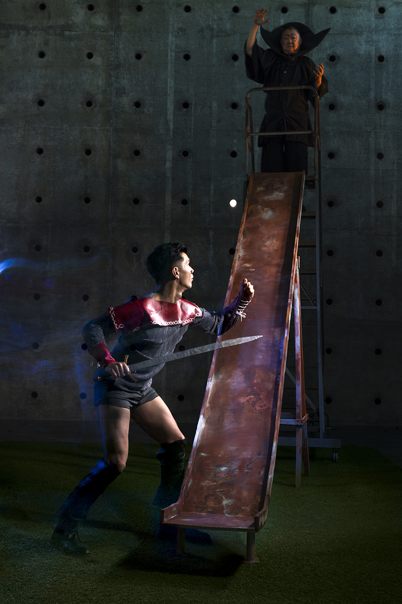 Actors dressed as Flash Gordon and Ming the Merciless confront each other on a playground slide. 