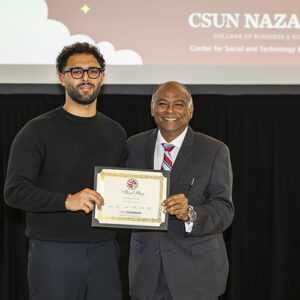 Two men stand side by side, holding a certificate, with a video screen behind them.