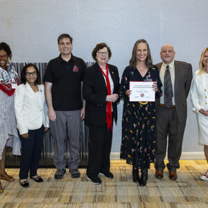 Seven people stand together, the person in the center holds a certificate.