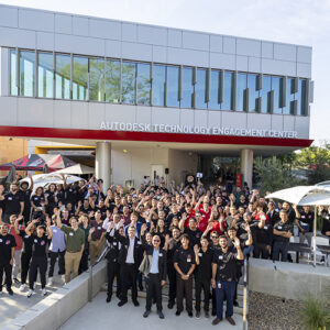 A large group of people stands outside the Autodesk Technology Engagement Center.