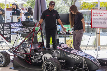 Two students stand behind a one-seater race car.