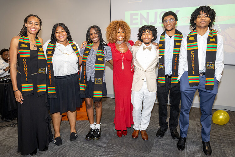 Students wearing colorful stoles and Theresa White stand together with their arms around each other.