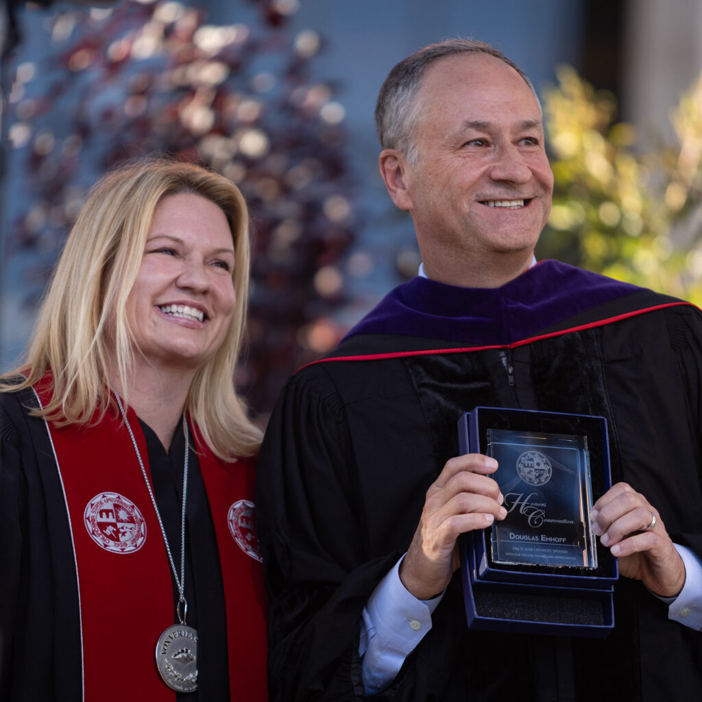 CSUN President Erika D. Beck and Doug Emhoff stand together on stage. Emhoff holds a glass plaque.