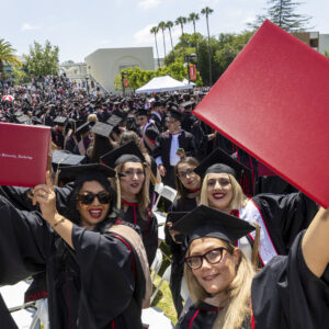 A group of CSUN graduates hold up their new diplomas on the University Library Lawn.
