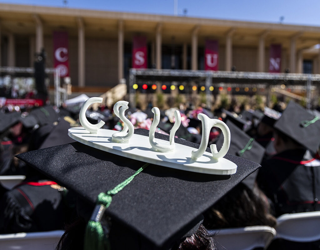 A small sculpture spelling CSUN adorns a mortarboard at a graduation ceremony.