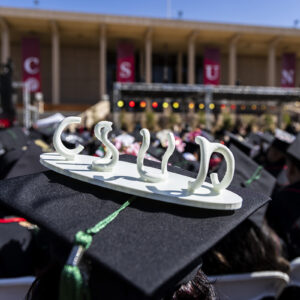 A small sculpture spelling CSUN adorns a mortarboard at a graduation ceremony.