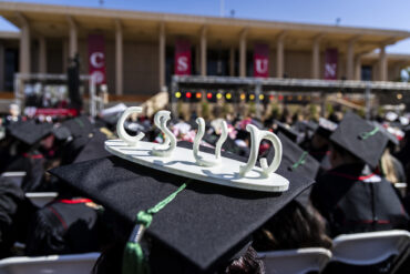 A small sculpture spelling CSUN adorns a mortarboard at a graduation ceremony.