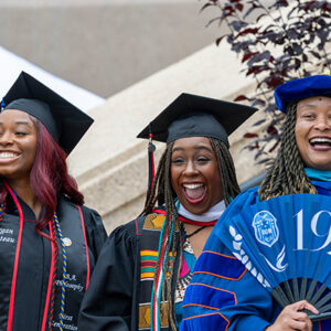 Three people in graduation regalia smile and celebrate during Black Graduation.