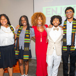 Students wearing colorful stoles and Theresa White stand together with their arms around each other.