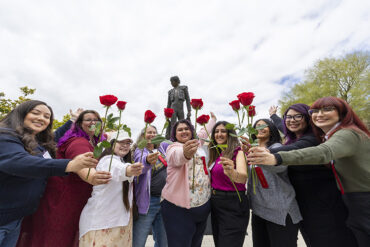 A group of people stand in front of the Matador statue, each person holds up a red rose.
