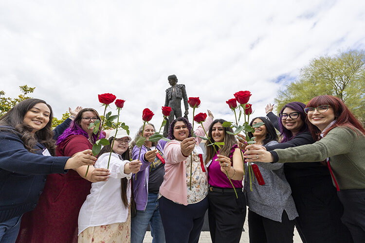 A group of people stand in front of the Matador statue, each person holds up a red rose.