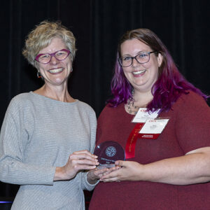 Two people stand together, smiling and holding a glass award.
