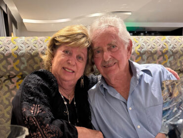 Carol and Art Altshiller sit close on a couch.