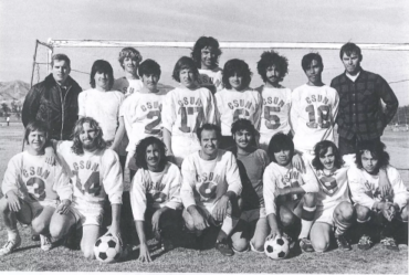 Black-and-white photo of CSUN men's club soccer team, wearing uniforms and lined up in two rows in front of a soccer goal.