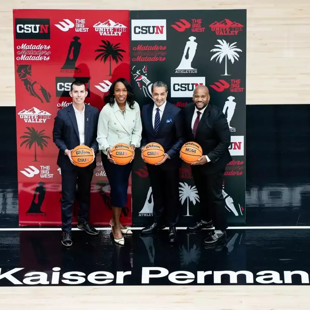 Four people holding basketballs in front of an Athletics sign