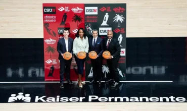 Four people holding basketballs in front of an Athletics sign