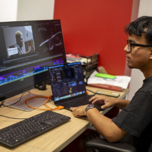 David Ajtun sits at a desk before a computer monitor displaying a video editing project.