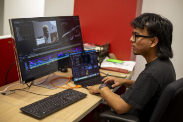 David Ajtun sits at a desk before a computer monitor displaying a video editing project.