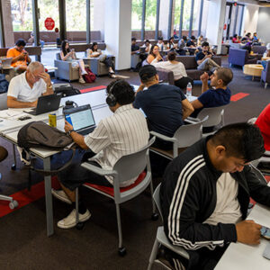 Student seated at tables, some with laptops open.