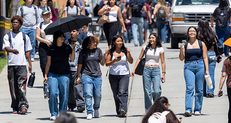 Three smiling women in foreground with crowds of people in the background.