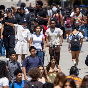 A crowd of students wearing backpacks on a campus sidewalk.